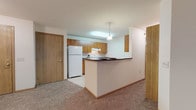 Located at 6530 Schroeder Rd in Madison, Wisconsin, this single-floor unit offers a functional and well-organized layout designed for comfortable everyday living. The open living and dining area is generously sized, finished with warm neutral carpet and served by a pendant light fixture, creating a bright and welcoming atmosphere. Vertical blinds on a sliding door provide access to natural light and outdoor views. The kitchen features a peninsula with a dark countertop that opens toward the living space, offering a practical pass-through design ideal for casual dining or entertaining. Warm wood-toned cabinetry lines the kitchen walls, complemented by white appliances including a refrigerator and electric range, and tile flooring for easy maintenance. Two carpeted bedrooms provide comfortable retreats, each with windows fitted with blinds. One bedroom benefits from elevated windows that allow additional natural light to filter in, while a walk-in closet adds useful storage. Both bathrooms are finished with light tile flooring, wood-toned vanity cabinetry, and tub-shower combinations. The overall design emphasizes practicality with consistent warm wood finishes and neutral tones carried throughout the space.