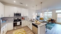 Located at 2723 South Blvd in Charlotte, NC, this single-floor residence showcases a thoughtfully designed open-concept layout with modern finishes throughout. The kitchen serves as a central highlight, featuring white shaker cabinetry, granite countertops, a subway tile backsplash, and a full suite of stainless steel appliances, including a range, microwave, and dishwasher. A peninsula island with pendant lighting provides additional prep space and casual seating, flowing seamlessly into the living area, which benefits from natural light through large windows with outdoor views.

The bedroom is generously proportioned, offering plush carpeting, dual windows that invite natural light, and a ceiling fan. It connects directly to a well-appointed bathroom featuring a granite-topped vanity with dark cabinetry and a large framed mirror. Adjacent to the bathroom, a spacious walk-in closet provides ample storage with shelving and hanging space.

Wood-style plank flooring runs throughout the main living areas, complementing the clean, neutral color palette. Recessed lighting and modern fixtures add a polished finish. The overall ambiance is bright, clean, and contemporary, reflecting a well-designed urban living space in the heart of Charlotte.