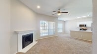 This single-floor home offers a thoughtfully designed open layout that seamlessly connects the living, dining, and kitchen areas. The spacious living room is a standout, featuring vaulted ceilings, a ceiling fan with light fixture, a classic white-mantled fireplace with shiplap surround, and large windows fitted with blinds that invite generous natural light. The open-concept kitchen is equipped with stainless steel appliances — including a range, over-the-range microwave, and refrigerator — complemented by crisp white cabinetry and a peninsula with a built-in sink, providing both workspace and a natural divider from the living area. Light wood-look flooring anchors the kitchen, while plush neutral carpeting extends throughout the living spaces and bedrooms. The bedrooms are well-sized, each featuring ceiling fans and windows that allow natural light to filter in. The bathroom is clean and functional, appointed with a white vanity, framed mirror, and a tiled tub-shower combination. A dedicated laundry area with an in-unit washer and dryer adds everyday convenience. Overhead shelving in the laundry space provides additional storage. The home's neutral palette and open design create a bright, comfortable living environment throughout.