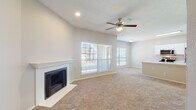 This single-floor home offers a thoughtfully designed open layout that seamlessly connects the living, dining, and kitchen areas. The spacious living room is a standout, featuring vaulted ceilings, a ceiling fan with light fixture, a classic white-mantled fireplace with shiplap surround, and large windows fitted with blinds that invite generous natural light. The open-concept kitchen is equipped with stainless steel appliances — including a range, over-the-range microwave, and refrigerator — complemented by crisp white cabinetry and a peninsula with a built-in sink, providing both workspace and a natural divider from the living area. Light wood-look flooring anchors the kitchen, while plush neutral carpeting extends throughout the living spaces and bedrooms. The bedrooms are well-sized, each featuring ceiling fans and windows that allow natural light to filter in. The bathroom is clean and functional, appointed with a white vanity, framed mirror, and a tiled tub-shower combination. A dedicated laundry area with an in-unit washer and dryer adds everyday convenience. Overhead shelving in the laundry space provides additional storage. The home's neutral palette and open design create a bright, comfortable living environment throughout.