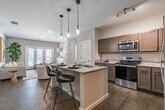 Located at 16000 Rushmore Avenue in Little Rock, AR, this single-floor, 2-bedroom, 2-bathroom residence offers a thoughtfully designed open-concept layout with modern finishes throughout. Dark hardwood-style flooring flows continuously through the main living areas, anchoring a neutral, light-filled color palette.

The kitchen is a standout feature, boasting taupe cabinetry, granite countertops, stainless steel appliances, and a central island with seating for two, illuminated by a trio of pendant lights. The kitchen opens seamlessly to the living room, which features French doors that invite natural light and provide access to an outdoor space.

The primary bedroom is a comfortable retreat with large windows, a closet, and direct access to a private bathroom. The second bedroom also benefits from generous natural light and hardwood-style flooring. Both bathrooms are finished with granite-topped vanities and warm cabinetry, with one featuring a full tub-shower combination.

A dedicated laundry room houses a full-size side-by-side washer and dryer, adding everyday convenience. Throughout the residence, clean architectural lines, recessed lighting, and a cohesive neutral palette create a modern yet welcoming ambiance.