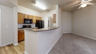 Located at 1750 Village Commons Dr in Conway, AR, this one-bedroom, one-bathroom residence offers a practical and well-organized single-floor layout. The entrance leads into a galley-style kitchen outfitted with warm honey-toned cabinetry, granite-look countertops, black appliances including a refrigerator, range, microwave, and dishwasher, and wood-look plank flooring. A curved breakfast bar peninsula separates the kitchen from the combined dining and living area, which features plush carpeting, a ceiling fan, a pendant light fixture, and multiple windows that bring in natural light and views of the surrounding greenery. The bedroom is a comfortable size, featuring vaulted ceilings, carpeted flooring, and dual windows that further enhance the sense of openness and light. Two closets provide ample storage throughout the unit. The bathroom includes warm wood-toned cabinetry with a granite-look vanity top and wood-look plank flooring. A dedicated laundry area adds everyday convenience. Neutral tones and consistent finishes throughout the space create a cohesive and inviting atmosphere well-suited for comfortable living.
