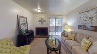 This single-floor residence presents a well-organized layout that connects key living areas in a practical and comfortable arrangement. The living room serves as the central gathering space, featuring a brick-surround fireplace as a focal point, soft wall-to-wall carpeting, and a large sliding glass door fitted with vertical blinds that allows natural light to filter in and provides outdoor access.

Adjacent to the living room, the dining area accommodates a round table beneath a pendant light fixture, with a pass-through counter connecting to the kitchen for added convenience. The galley-style kitchen is efficiently designed with warm oak cabinetry, light butcher-block-style countertops, tile flooring, and a full suite of appliances including a refrigerator, electric range, built-in microwave, and dishwasher. Ample upper and lower cabinet storage ensures practical functionality.

The bedroom is a calm, carpeted retreat with a window offering views of surrounding greenery and a closet with a full-panel door. The bathroom features tile flooring, a shower-tub combination, and a vanity with built-in storage. Throughout the unit, neutral wall tones and consistent finishes create a cohesive and inviting atmosphere.