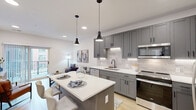 Located at 100 Mia Rose Way in Dardenne Prairie, MO, this well-appointed one-bedroom, one-bathroom residence offers a thoughtfully designed layout across a single floor. The open-concept kitchen is a standout feature, showcasing sleek gray shaker-style cabinetry with under-cabinet lighting, a light subway tile backsplash, white quartz countertops, stainless steel appliances, and a central island with seating — all illuminated by stylish black pendant lights. The kitchen flows seamlessly into the living area, which is bright and airy thanks to a sliding glass door that opens onto a private balcony. Light wood-style flooring runs throughout, lending warmth and continuity to the space. The bedroom is a comfortable retreat with neutral tones, a ceiling fan, and access to generous closet storage, including well-organized built-in shelving. The bathroom features a gray vanity with quartz countertop and a backlit mirror that adds a modern, refined touch, alongside a tiled shower. Additional highlights include in-unit laundry, a hallway connecting all areas efficiently, and multiple closets providing ample storage throughout this clean, contemporary residence.