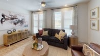This single-floor residence is designed with an open, contemporary layout that connects the kitchen, dining, and living areas into one cohesive space. The kitchen serves as a central hub, featuring a large island with seating for several, white upper cabinetry paired with dark lower cabinets, a marble-style backsplash, stainless steel appliances, and track lighting overhead. Light wood-style flooring runs throughout these shared spaces, enhancing the bright, airy feel.

The living room benefits from an abundance of natural light provided by multiple large windows dressed with patterned drapes and wood blinds. A ceiling fan adds comfort to the space. Adjacent to the living area, the dining space accommodates a full-sized table and also features generous window exposure.

The primary bedroom is well-proportioned, carpeted, and receives natural light through a large window. Its en-suite bathroom includes wood-look flooring, a single-sink vanity with dark cabinetry and a white countertop, a toilet, and a tub-shower combination with tile surround. A walk-in closet connects directly to this bathroom. The second bedroom is similarly carpeted and bright, served by a full bathroom with matching finishes.