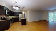 This single-floor residence offers a thoughtfully designed layout that balances open living spaces with private retreats. The heart of the home is an open-concept kitchen and living area, unified by warm hardwood-style flooring. The kitchen is well-equipped with dark espresso cabinetry, granite countertops, stainless steel appliances including a refrigerator, range, microwave, and dishwasher, and a decorative tile backsplash. A central island with a granite surface provides additional workspace and casual seating. Pendant lighting adds a polished finishing touch above both the island and the main kitchen area. The living area flows generously from the kitchen, offering ample room for furnishing and entertaining. The bedrooms feature neutral carpet, large windows with blinds that invite natural light, and individual climate control units along with baseboard heating. Two bathrooms serve the residence: one features a tiled tub-shower combination with light stone-look tile and a dark vanity with a granite countertop, while the second offers a glass-enclosed walk-in shower, a matching dark vanity, and elegant large-format tile flooring. Clean white walls and simple, consistent finishes throughout create a cohesive and inviting ambiance.