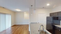 This single-floor residence offers a thoughtfully designed layout that balances functionality and comfort throughout its living spaces. The kitchen serves as a central highlight, featuring dark espresso-toned cabinetry with brushed nickel hardware, speckled stone countertops, a stainless steel sink, and a full suite of black appliances including a refrigerator, electric range, built-in microwave, and dishwasher. A peninsula counter with pendant lighting creates a natural transition into the open dining area, which connects seamlessly to the living room. The living area is warm and inviting, with rich hardwood-style flooring, a ceiling fan with light fixture, and large windows alongside a sliding glass door dressed with vertical blinds that allow for generous natural light and outdoor views. A carpeted bedroom provides a quiet retreat, complete with a window offering neighborhood views. The bathroom features a soaking tub and shower combination with white tile surround and chrome fixtures. Neutral wall tones and clean white trim are consistent throughout the space, creating a cohesive and move-in-ready aesthetic that is both practical and welcoming.