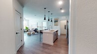 This single-floor residence is designed with a contemporary aesthetic, blending open-concept living with well-defined functional spaces. The kitchen serves as a central hub, anchored by a large island with a light quartz countertop and an integrated sink, accommodating seating for two. Three striking cone-shaped pendant lights hang above the island, complementing the soft-toned cabinetry, geometric tile backsplash, and a full suite of stainless steel appliances. Wood-look flooring extends throughout the main living areas, adding warmth and cohesion. An arched doorway adds an architectural detail that transitions the kitchen toward additional spaces, including an in-unit laundry room.

The living room is bright and inviting, with large windows allowing generous natural light and crown molding adding a refined touch. Two bedrooms offer comfortable retreats; one features a bold teal accent wall and natural light from a large window, while the other is finished in neutral tones with plush carpet and a ceiling fan.

The bathroom is well-appointed, featuring a dual-sink vanity with a light countertop, gray cabinetry, a glass-enclosed shower-tub combination, and wood-look flooring — with direct access to the primary bedroom.