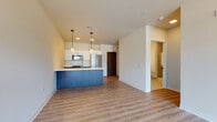Located in Milwaukee's desirable East Side neighborhood, this contemporary single-floor unit offers a thoughtfully designed open-concept layout with modern finishes throughout. The kitchen serves as a central focal point, featuring a striking blue island with a dark countertop, white upper cabinetry, a subway tile backsplash, and stainless steel appliances including a refrigerator, range, and over-the-range microwave. Warm-toned luxury vinyl plank flooring extends through the main living areas, creating a cohesive and inviting atmosphere. The living area is bathed in natural light and provides direct access to a private balcony through expansive floor-to-ceiling sliding glass doors, offering views of the surrounding neighborhood and the Milwaukee skyline beyond. The bedroom features plush carpeting and a tall, narrow window that brings in additional natural light, while a dedicated walk-in closet with built-in wire shelving provides generous storage. The bathroom is finished with large-format tile flooring, a dark navy vanity with a white countertop, a backlit mirror, and a glass-enclosed walk-in shower adorned with textured tile surround. Clean lines, neutral tones, and contemporary fixtures give the entire space a polished, move-in-ready appeal.