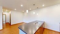 Located in Spokane Valley, WA, this well-appointed three-bedroom, two-bathroom residence offers a thoughtfully designed single-level layout. The open-concept living area seamlessly combines the kitchen, dining, and living spaces into one generous, light-filled room. The kitchen is anchored by a large island with a dark laminate countertop, double stainless steel sink, and warm wood cabinetry, all illuminated by a trio of pendant lights overhead alongside recessed ceiling lighting. Hardwood-style flooring flows throughout the main living areas, adding warmth and continuity to the space.

The three bedrooms offer a comfortable retreat, with the primary bedroom providing a generous footprint and ample closet storage. Carpeted floors add comfort to the sleeping areas, which also feature natural light through slatted blinds. The two bathrooms are clean and functional, featuring wood-tone cabinetry, white countertops, and a tub-shower combination. Baseboard heating is present throughout the unit.

Additional conveniences include four closets, a dedicated laundry area, and a hallway connecting the rooms efficiently. A private balcony offers open views of the surrounding Spokane Valley community and the distant hillside horizon under expansive Pacific Northwest skies.