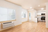 This single-floor unit offers a clean, functional layout designed for comfortable everyday living. The open-concept living area is bright and airy, featuring light hardwood-style flooring, neutral beige walls, and multiple windows fitted with blinds that allow natural light to filter in. A wall-mounted PTAC heating and cooling unit provides climate control directly in the living space, complemented by a wall thermostat nearby.

The kitchen is well-equipped with stainless steel appliances, including a refrigerator, electric range, and over-the-range microwave. White cabinetry extends to the ceiling, offering generous storage, while light granite-style countertops add a polished finish. The kitchen flows naturally toward a door providing outdoor access.

The bedrooms are carpeted in a neutral tone, each featuring a window with natural light and individual PTAC units for personalized comfort. The rooms offer a versatile, open canvas for furnishing.

Two bathrooms serve the unit. One features a sliding frosted-glass shower enclosure, a toilet, and a stone-patterned vanity countertop. The second is a more compact space with a grab bar and ventilation unit, suggesting accessible design considerations.

Throughout the unit, light wood-toned baseboards, recessed lighting, and a consistent neutral palette create a cohesive, understated aesthetic.