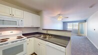 Located at 650 Woodward St in San Marcos, California, this single-floor residence offers a practical and comfortable layout designed for everyday living. The kitchen is well-equipped with white cabinetry, dark laminate countertops, a double-basin sink, and a full suite of white appliances including a refrigerator, electric range, over-the-range microwave, and dishwasher. Wood-look flooring in the kitchen adds a clean, durable finish. A peninsula counter opens the kitchen toward the living area, creating a connected, open feel. The carpeted living room is bright and generously sized, featuring a ceiling fan with integrated lighting and a window that allows natural light to filter in. The bedrooms continue the same soft carpet flooring and neutral wall tones, each equipped with a ceiling fan and window, lending the rooms a calm, airy atmosphere. The bathroom is finished with wood-look vinyl flooring, a white vanity with dark countertop, a full tub-shower combination with white tile surround and safety grab bars, and a large mirror. Throughout the residence, a consistent palette of soft grays and whites creates a cohesive, understated aesthetic suited to comfortable, low-maintenance living in the San Marcos community.
