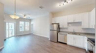 This single-story residence offers a thoughtfully designed layout across two bedrooms and two bathrooms. The open-concept living and kitchen area forms the heart of the home, where wood-style plank flooring flows seamlessly underfoot and neutral-toned walls create a bright, welcoming atmosphere. The living room benefits from generous natural light through large windows and a sliding glass door that opens to a private balcony, complemented by a ceiling fan overhead.

The kitchen is well-equipped with white shaker-style cabinetry extending to the ceiling for ample storage, granite-look countertops, a subway tile backsplash, and a full suite of stainless steel appliances including a refrigerator, dishwasher, range, and microwave. Track lighting illuminates the workspace effectively.

Both bedrooms feature plush carpeting, ceiling fans, and windows with blinds. The primary bedroom is a comfortable size and includes access to a walk-in closet outfitted with wire shelving systems. The bathrooms feature white cabinetry, granite-look countertops, and tub-shower combinations with clean white tile surrounds and wood-style flooring, maintaining a consistent, modern aesthetic throughout.