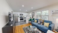 Located at 96 E Lakeview Ave in Leonia, NJ, this well-appointed one-bedroom, one-bathroom unit offers a thoughtfully designed layout that maximizes every square foot. The open-concept living and kitchen area serves as the heart of the home, where warm hardwood floors in the living space transition to large-format slate-toned tile in the kitchen. The kitchen is outfitted with stainless steel appliances, crisp white shaker cabinets, light countertops, and a peninsula with bar seating — ideal for casual dining or entertaining. Multiple windows throughout the living area flood the space with natural light and offer lush, tree-lined outdoor views. The bedroom is a comfortable and serene retreat, featuring hardwood floors, crown molding, multiple windows with outdoor views, and ample closet access via the adjoining hallway. The bathroom is elegantly finished with marble-style tile surround in the tub-shower combination, a gray vanity with matte black fixtures, and a framed mirror. Additional highlights include in-unit laundry, two closets for storage, and a staircase providing building access. The unit's clean, neutral palette and modern updates create a move-in-ready living environment.