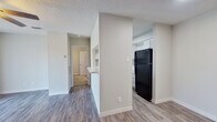 This well-designed single-floor unit offers a thoughtful layout that makes efficient use of its intimate footprint. The living room features durable wood-look flooring, a ceiling fan with light fixture, a textured ceiling, and a sliding glass door with vertical blinds that allows natural light to fill the space. Adjacent to the living area, the kitchen is accessible via a convenient pass-through counter opening, and is equipped with white cabinetry, a black refrigerator, and a sink — keeping the space functional and bright with a clean, neutral palette throughout.

A short hallway connects the main living area to the private quarters. The bedroom is carpeted for comfort and includes a ceiling fan, a window with blinds that invites natural light, and clean, neutral-toned walls. The bedroom is complemented by a generously sized walk-in closet outfitted with multiple shelving tiers and hanging rods on three walls, offering ample storage and organization options.

The full bathroom features wood-look flooring consistent with the rest of the unit, a full soaking tub with a shower and tiled surround, a toilet, and a vanity with a stone-look countertop. Throughout the unit, light gray walls and clean white trim create a cohesive, modern aesthetic that feels fresh and move-in ready.