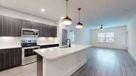 This thoughtfully designed 2-bedroom, 2-bathroom residence spans a single floor and features a clean, contemporary aesthetic throughout. Light gray wood-look flooring flows consistently across the entire space, creating a cohesive and modern foundation.

The open-concept kitchen and living area serves as the heart of the home. The kitchen is outfitted with dark textured cabinetry, crisp white quartz countertops, a full suite of stainless steel appliances—including a French door refrigerator, range, and microwave—and a generous island with an undermount sink. Brass pendant lights hang above the island, adding a warm, stylish contrast. The adjacent living area features a ceiling fan and large windows that allow ample natural light to fill the space.

Both bedrooms are well-proportioned and bright, each featuring ceiling fans, large windows with exterior views, and neutral white walls that lend a clean, airy feel. The primary bedroom includes a dedicated walk-in closet outfitted with wire shelving for organized storage.

The bathrooms continue the modern design language, featuring dark-finished hardware, wood-toned vanity cabinetry, white quartz countertops, and a tiled tub-shower combination with subway tile surround. Light wood-look flooring extends into the bathrooms, maintaining design consistency throughout the residence.