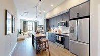 Located at 2141 Waterside Drive in Nashville, TN, this thoughtfully designed one-bedroom, one-bathroom residence offers a smart, efficient layout that maximizes every inch of its well-proportioned floor plan. The open-concept living and kitchen area creates a seamless flow, anchored by a modern kitchen featuring slate-blue cabinetry with matte black hardware, white subway tile backsplash, stainless steel appliances, and a central island with bar seating illuminated by stylish pendant lighting. Light wood-tone flooring runs throughout, enhancing the bright, airy feel of the space. The living room is generously sized with large windows that invite abundant natural light and frame expansive outdoor views. The bedroom is a tranquil retreat with a large picture window overlooking open green scenery, complemented by soft neutral tones and plush carpeting. A dedicated closet provides ample storage. The bathroom is well-appointed with navy cabinetry, a quartz countertop, matte black fixtures, a tub-shower combination with white tile surround, and a graphic accent wall that adds a touch of personality. Recessed lighting throughout ensures a clean, contemporary ambiance across the entire residence.