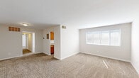 This single-floor unit offers a clean, functional layout designed to maximize usable living space. The open living area is generously proportioned, featuring neutral-toned wall-to-wall carpeting and crisp white walls that create a bright, airy atmosphere. A large window allows natural light to fill the room, while a centrally located HVAC vent ensures year-round comfort. The entry door opens directly into this expansive main living space, providing an open and welcoming feel.

The kitchen is conveniently positioned adjacent to the living area and features warm honey-toned wood cabinetry with ample upper and lower storage. A double-basin stainless steel sink, light-toned laminate countertops, and a white gas range with oven complete the space. Light wood-style vinyl flooring in the kitchen provides a practical contrast to the carpeted living areas.

The bedrooms are well-sized, each featuring neutral carpet, windows with blinds for natural light and privacy, and ceiling-mounted light fixtures. Storage is well addressed, with each bedroom offering dedicated closet space fitted with hanging rods. The bathroom includes a white vanity with sink, a mirror, and a tub-shower combination with tiled surround, finished in a clean, all-white palette.