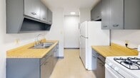 Located at 1072 Eastway Dr in Youngstown, Ohio, this single-floor unit offers a straightforward, functional layout with clearly defined living, sleeping, and kitchen areas. The galley-style kitchen is equipped with gray cabinetry above and below the counters, warm wood-tone laminate countertops, a stainless steel sink, a white gas range, and a full-size refrigerator. Vinyl tile flooring runs throughout the kitchen, which is illuminated by a flush ceiling light. The living area is generously sized, featuring neutral carpet, white walls, and multiple windows fitted with blinds that allow ample natural light and outdoor views of surrounding greenery. Baseboard heating runs along the perimeter of the living space. The bedroom is similarly carpeted and naturally lit through a window overlooking the exterior, with baseboard heating and access to a closet. The bathroom includes a full-size soaking tub with a shower, panel surround, and a small frosted window for ventilation and light. Throughout the unit, the clean, neutral palette and practical finishes create a simple, livable environment suited to everyday comfort.
