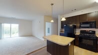 This single-floor residence at 15 Abbey Ln in Danbury, Connecticut offers a well-designed open-concept layout that seamlessly connects the kitchen and living areas. The kitchen is a standout feature, outfitted with rich dark espresso cabinetry, light countertops, a full suite of black appliances including a gas range, built-in microwave, and refrigerator, and a center island with pendant lighting overhead. Light hardwood-style flooring runs throughout the kitchen and entry areas, transitioning into plush neutral carpeting in the living and bedroom spaces.

The spacious living area is bright and airy, benefiting from a sliding glass door that invites natural light and provides views of the surrounding greenery. A dedicated entryway includes a closet, offering practical storage upon arrival. The bedrooms are comfortably sized with soft carpeting and large windows framing lush outdoor views of trees and landscaping. Ample closet space is present throughout.

The bathroom is finished with warm beige tile flooring, dark vanity cabinetry, a single-sink vanity with a large mirror, and a full soaking tub with shower. Clean white walls and neutral tones throughout the residence create a bright, move-in-ready atmosphere well-suited for comfortable everyday living.