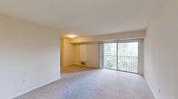 Located in Triangle, VA, this well-organized three-bedroom, two-bathroom residence offers a comfortable and practical layout across a single floor. The open living room serves as the heart of the home, featuring plush wall-to-wall carpeting, neutral warm-toned walls, and a large sliding glass door that leads to a private balcony with lush, tree-lined views, filling the space with natural light. The kitchen is efficiently designed with warm oak cabinetry extending to the ceiling for generous storage, dark granite-style countertops, hardwood-style flooring, and white appliances including a refrigerator and dishwasher. Three carpeted bedrooms provide comfortable accommodations, each with closet access — four closets are distributed throughout the unit. The primary bedroom offers a private, well-proportioned retreat. Both bathrooms are clean and functional; one features a full tub-shower combo with white tile surround and chrome fixtures, while the second offers a more compact layout with wood-look flooring. A connecting hallway ties the layout together efficiently. The overall aesthetic is understated and move-in ready, with a consistent neutral palette and natural light flowing throughout the space.