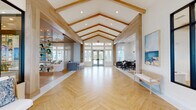 Located at 1900 Elevate Ave in Navarre, Florida, this single-story amenity clubhouse is designed with a refined coastal aesthetic throughout. The grand entrance foyer sets the tone with soaring vaulted ceilings accented by natural wood beams, herringbone-patterned light wood flooring, and floor-to-ceiling glass doors that flood the space with natural light. A welcoming seating area near the entrance is framed by black-framed glass walls and lush tropical greenery.

The main lounge offers a relaxed, resort-style atmosphere with a slatted wood ceiling, plush neutral furnishings, a decorative tiled accent wall with a mounted TV, and open shelving adorned with trailing plants. Adjacent to the lounge, a dining area features dark furniture, coastal artwork, and warm accent lighting.

A fully equipped fitness center provides an array of cardio and strength-training equipment, large windows overlooking the outdoors, and a wood-paneled ceiling that maintains the building's warm design language. A glass-enclosed conference room with pendant lighting and rattan seating offers a polished meeting environment, while a striking moss wall with an integrated display screen serves as a bold focal point.

The facility also includes a dedicated pet spa, featuring built-in washing stations, patterned tile flooring, and playful mosaic dog-themed wall art — a thoughtful amenity for residents and their pets.