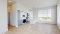 This well-appointed 2-bedroom, 2-bathroom residence offers a thoughtfully designed single-level layout with modern finishes throughout. The open-concept kitchen and living area serves as the heart of the home, featuring high ceilings, light-toned hardwood-style flooring, and a ceiling fan that enhances the airy atmosphere. The kitchen is outfitted with two-tone cabinetry — white upper cabinets paired with muted blue-grey lower cabinets — complemented by a white subway tile backsplash, stainless steel appliances including a refrigerator with ice dispenser, microwave, and range, and a spacious kitchen island with a quartz countertop and undermount sink. Large windows flood the living area with abundant natural light and frame elevated views of the surrounding cityscape and tree canopy. Both bedrooms are carpeted and generously proportioned, with the primary bedroom featuring a walk-in closet equipped with wire shelving systems. The bathrooms are finished with wood-look flooring and include a soaking tub and shower with a herringbone-patterned white tile surround. The clean, neutral color palette and contemporary design choices create a bright, cohesive living environment throughout the entire space.