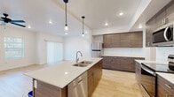 Located at 14367 S Bella Vea Dr in Herriman, Utah, this contemporary two-story home showcases a clean, modern design throughout its well-appointed interior. The open-concept kitchen serves as the heart of the main level, featuring a large central island with a double basin sink, crisp white quartz countertops, and wood-grain cabinetry in a warm walnut-toned finish. Stainless steel appliances—including a refrigerator, electric range, built-in microwave, and dishwasher—complement the space, while stylish pendant lights hang above the island. Light hardwood-style flooring flows throughout the main living areas, enhancing the bright, airy atmosphere. The living area extends naturally from the kitchen, offering a ceiling fan, recessed lighting, and a sliding glass door that welcomes natural light. Bedrooms feature plush carpeting, ceiling fans, and windows with horizontal blinds that frame neighborhood views. Bathrooms are finished with wood-tone floating vanities, white quartz countertops, undermount sinks, and tub-shower combinations. The attached garage provides generous space with a concrete floor, drywall-finished walls, and overhead lighting—offering ample room for vehicles and storage. The overall design palette of whites, neutrals, and warm wood tones gives the home a cohesive, contemporary feel.