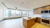 Located in the heart of Dallas, TX, this single-floor unit at 1407 Elm St offers a sleek, contemporary design with a well-thought-out layout. The open-plan kitchen and living area forms the centerpiece of the space, featuring warm walnut-toned cabinetry, quartz countertops, and a full suite of stainless steel appliances, including a gas range, built-in microwave, dishwasher, and a French door refrigerator. Light bamboo hardwood flooring runs throughout the main living areas, complementing the clean white walls and recessed lighting overhead. A kitchen island with an undermount sink adds both functionality and style.

The living area is bathed in natural light, with expansive floor-to-ceiling windows framing breathtaking panoramic views of the Dallas skyline, including the iconic Fountain Place tower. The bathroom is elegantly appointed with a dual-sink vanity featuring soft blue cabinetry, marble-tiled walls, large-format tile flooring, and a frameless glass walk-in shower. A dedicated walk-in closet offers built-in shelving and dual hanging rods, providing ample storage. The entry foyer transitions smoothly into the main living space, completing a unit that balances modern urban living with refined, functional design.