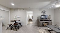 This efficiently designed 1-bedroom, 2-bathroom single-story unit offers a thoughtful layout across a compact but functional footprint. Light wood-style flooring flows consistently throughout, lending a clean, cohesive look to the entire space.

The living room serves as the heart of the unit, featuring a ceiling fan, a window dressed with sheer curtains that allow natural light to filter in, and enough room to accommodate a full sofa arrangement and media console. A small dining area sits adjacent, ideal for casual meals.

The galley kitchen is well-equipped with gray cabinetry, white countertops, a tiled backsplash, and stainless steel appliances including a refrigerator, range, and microwave. The dual-counter layout maximizes workspace and storage efficiency.

The primary bedroom is a comfortable retreat, featuring a ceiling fan, a window with blinds, and enough space for a full bedroom suite. It connects directly to a private bathroom with a tub-shower combination, a single vanity with a large mirror, and access to a dedicated walk-in closet complete with overhead shelving and hanging rods. A second bathroom serves guests and provides additional convenience.

Neutral gray-toned walls throughout create a calm, modern ambiance that complements the rustic and contemporary decorative accents visible across the space.