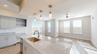 Located at 5222 Shadydell Dr in Fort Worth, TX, this single-story, 2-bedroom, 2-bathroom home offers a thoughtfully designed open-concept layout filled with natural light. The combined living, dining, and kitchen area serves as the heart of the home, where light hardwood-style flooring, ceiling fans, and large windows create a bright, airy atmosphere. The kitchen is a standout feature, boasting granite countertops, a large island with a undermount sink and pendant lighting, gray shaker-style cabinetry, open shelving, stainless steel appliances, and ample counter space. Both bedrooms are carpeted and generously sized, with the primary bedroom offering a ceiling fan, a wide window with natural light, and access to its own bathroom. The primary bath features a granite vanity, gray cabinetry, and a large framed mirror. Closets include well-organized built-in shelving and hanging rods. Additional spaces include a dedicated laundry area, a pantry, and multiple hallways connecting the layout seamlessly. Neutral tones, clean white trim, and consistent finishes throughout lend the home a modern, move-in-ready appeal.