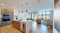 Located at 13125 Watertown Plank Road in Elm Grove, Wisconsin, this thoughtfully designed 2-bedroom, 3-bathroom residence offers a modern aesthetic with high-quality finishes throughout. The open-concept living area seamlessly connects the kitchen, dining room, and living room, all bathed in abundant natural light from expansive floor-to-ceiling windows with sleek black frames that frame outdoor views. The kitchen is a standout feature, boasting two-tone cabinetry with warm wood lower cabinets and crisp white uppers, a gas cooktop, stainless steel wall ovens, a statement range hood, and a large island with pendant lighting — ideal for both cooking and entertaining. The dining area sits adjacent to a glass door leading to the private patio, enhancing the indoor-outdoor flow. The living room features built-in wood shelving and generous wall-to-wall windows. The spacious primary bedroom offers plush carpeting, ample natural light, and a well-appointed en-suite bathroom with a double vanity and a glass-enclosed shower. The second bedroom is bright and comfortable with its own closet. Three full bathrooms, in-unit Whirlpool laundry, and multiple closets complete this refined and functional residence.