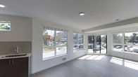 This contemporary single-floor space offers a clean, minimalist aesthetic defined by its open layout and bright, airy atmosphere. Large street-facing windows dominate the exterior walls, flooding the interior with generous natural light throughout the day while providing clear views of the surrounding urban neighborhood. The windows are fitted with roller shades, offering flexible light and privacy control as needed.

The space features smooth white walls and light-toned hardwood-style flooring that enhances the sense of openness and contributes to the modern, polished look. Recessed ceiling lighting complements the natural light, ensuring the interior remains well-illuminated at all hours. The ceiling is clean and flat, reinforcing the space's crisp, contemporary character.

The open floor plan offers a high degree of flexibility, making it well-suited for a variety of uses such as retail, a creative studio, or a professional office environment. Floor vents indicate a built-in climate control system for year-round comfort. The unobstructed layout allows for easy customization of the interior arrangement to suit a wide range of functional needs. Overall, the space presents a bright, welcoming environment with a strong street presence and a versatile, move-in-ready interior.