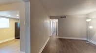 This single-floor space presents a straightforward and functional design characterized by a neutral, move-in-ready aesthetic. The flooring throughout consists of dark hardwood-style planks that provide a warm contrast against the crisp white baseboards lining the walls. The walls are finished in a soft taupe tone, lending a calm and versatile backdrop suitable for a variety of interior styles.

A central hallway connects the main areas of the space, offering clear sightlines through to additional rooms visible in the background. White-trimmed doorways frame the transitions between spaces, maintaining a cohesive and tidy appearance throughout. A ceiling-mounted light fixture illuminates the hallway, ensuring adequate lighting in the interior corridor.

The ceilings feature a textured finish and include a ceiling-mounted HVAC vent, indicating a central air system for climate control. Light switch plates are positioned at standard heights along the walls. The overall ambiance of the space is clean, neutral, and practical, making it well-suited for customization to personal taste while maintaining a functional and well-maintained foundation.