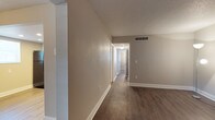 This single-floor space presents a straightforward and functional design characterized by a neutral, move-in-ready aesthetic. The flooring throughout consists of dark hardwood-style planks that provide a warm contrast against the crisp white baseboards lining the walls. The walls are finished in a soft taupe tone, lending a calm and versatile backdrop suitable for a variety of interior styles.

A central hallway connects the main areas of the space, offering clear sightlines through to additional rooms visible in the background. White-trimmed doorways frame the transitions between spaces, maintaining a cohesive and tidy appearance throughout. A ceiling-mounted light fixture illuminates the hallway, ensuring adequate lighting in the interior corridor.

The ceilings feature a textured finish and include a ceiling-mounted HVAC vent, indicating a central air system for climate control. Light switch plates are positioned at standard heights along the walls. The overall ambiance of the space is clean, neutral, and practical, making it well-suited for customization to personal taste while maintaining a functional and well-maintained foundation.