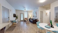 This well-designed single-floor residence offers a thoughtful layout that balances comfort and modern style. The open-concept living and dining area serves as the heart of the unit, featuring light wood-look flooring, neutral walls, and a ceiling fan that enhance the bright, airy atmosphere. Large windows allow natural light to fill the space, and a glass-paneled door provides access to the exterior. The living area is anchored by a tufted leather sofa and accented with bold abstract wall art, creating a welcoming and stylish environment.

The kitchen is outfitted with dark wood cabinetry, granite countertops, a classic white subway tile backsplash, and stainless steel appliances including a refrigerator, range, microwave, and dishwasher. A kitchen island with bar seating and pendant lighting above makes it ideal for casual dining and entertaining.

Two bedrooms offer plush carpeted flooring, soft neutral tones, and ample natural light. One bedroom includes a dedicated workspace with a wooden desk, while the other features generous room for a full furniture arrangement. Each bedroom is served by its own full bathroom, both finished with granite-topped dark wood vanities, tiled flooring, and a shower-tub combination.