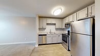 Located at 601 N Dupont Ave in Nashville, TN, this single-floor, one-bedroom, one-bathroom unit offers a thoughtfully arranged layout that maximizes every inch of its compact footprint. The kitchen is a functional highlight, featuring stainless steel appliances—including a refrigerator, range, microwave, and dishwasher—paired with light gray shaker-style cabinetry, granite-look countertops, and wood-look plank flooring. The kitchen opens seamlessly toward the living area, which transitions to soft carpeting, creating a clear distinction between the two zones. The bedroom is a comfortable, well-proportioned space with plush carpet, a ceiling fan with light fixture, a window that brings in natural light, and access to a dedicated closet. A hallway connects the main living spaces and provides access to the utility room, where an in-unit washer is conveniently tucked beneath a countertop. The bathroom features a full soaking tub and shower combo with built-in shelving. Neutral gray walls throughout the unit lend a clean, modern feel, while white trim and doors add crisp contrast. The overall ambiance is tidy, move-in ready, and well-suited for functional everyday living.
