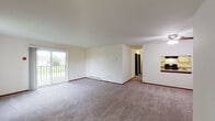 This single-floor unit offers a thoughtfully organized layout that balances open communal spaces with private retreats. The spacious living area is carpeted throughout and filled with natural light, courtesy of large sliding glass doors that open onto a private balcony with outdoor views of surrounding greenery. A ceiling fan overhead adds both functionality and a finished look to the room. A pass-through window connects the living area to the kitchen, creating an open, communicative flow between spaces.

The kitchen is efficiently designed in a U-shaped configuration, featuring white cabinetry with ample storage, laminate countertops, a double-basin sink, and black appliances including a range and refrigerator. Wood-style flooring runs throughout the kitchen, offering a clean contrast to the carpeted living and sleeping areas.

The bedrooms are generously sized, each with plush carpeting, baseboard heating, and windows that invite natural light and outdoor views. The rooms provide a calm, neutral environment well-suited for rest or a home office setup.

The bathroom is equipped with a wide vanity featuring a built-in sink and stone-look countertop, a full soaking tub with a shower, wood-style flooring, and a large louvered closet for additional storage. Throughout the unit, consistent neutral tones and clean finishes create a cohesive and inviting atmosphere.