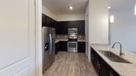 This single-story residence in Georgetown, Texas, offers a thoughtfully designed one-bedroom, one-bathroom layout with contemporary finishes throughout. The kitchen serves as a focal point of the home, showcasing dark espresso cabinetry paired with granite-look countertops, a neutral tile backsplash, and a full suite of stainless steel appliances, including a refrigerator with an in-door ice and water dispenser, an electric range, and a built-in microwave. Wood-look plank flooring runs through the kitchen and main living area, adding warmth and durability to the space.

The open living and dining area transitions seamlessly from the kitchen, illuminated by stylish pendant lighting that adds a modern touch. A hallway connects the main living space to the private bedroom, which features plush carpet flooring, a ceiling fan, and a window that brings in natural light. The bedroom is complemented by a spacious closet with a full-width hanging rod and shelving for ample storage.

The bathroom continues the home's cohesive design with light tile flooring, dark vanity cabinetry, granite-look countertops, and a bathtub with shower. The overall aesthetic is clean, neutral, and move-in ready.