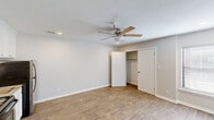 Located at 9524 E 71st St in Tulsa, Oklahoma, this single-floor unit offers a thoughtfully arranged layout comprising a living area and a full bathroom. The main living space is finished with warm wood-look laminate flooring that runs throughout, complemented by neutral gray-toned walls and clean white baseboards that create a bright, cohesive aesthetic. A ceiling fan with a light fixture is centrally mounted beneath a textured ceiling, providing both air circulation and ambient lighting, while recessed lighting adds additional illumination. A built-in kitchenette along one wall features white upper cabinetry, a stainless steel electric range, a refrigerator, and a sink with granite-style countertops — offering convenient cooking essentials in a compact footprint. A reach-in closet with shelving provides practical storage. A window with blinds allows natural light to fill the room. The bathroom is well-equipped with a large vanity topped with granite-style countertops, a wide mirror with overhead lighting, white cabinetry, and a walk-in shower stall fitted with grab bars for added accessibility. Tile flooring completes the bathroom's clean, functional design. Overall, the space presents a practical and comfortable environment suited to efficient, everyday living.