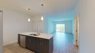 This single-floor residence at 13 N Wille St in Mount Prospect, IL offers a clean, contemporary design throughout. The open-concept layout connects the kitchen and living area seamlessly, creating a spacious, functional environment. The kitchen is a standout feature, centered around a large island with a white quartz countertop, an undermount sink, and dark charcoal cabinetry. Stainless steel appliances include a gas range, over-the-range microwave, French door refrigerator with ice maker, and a dishwasher. White upper cabinetry provides additional storage, and stylish pendant lighting adds a modern touch overhead. Light wood-style flooring runs throughout the unit, contributing to a bright, cohesive aesthetic. The living area benefits from natural light streaming through large sliding glass doors that open to an outdoor space. The bedrooms are well-proportioned, each featuring neutral white walls and natural light from windows. One bedroom includes a walk-in closet equipped with wire shelving. The primary bathroom offers a dual-sink vanity with quartz countertops, dark cabinetry, and a prominently lit backlit mirror. A secondary bathroom maintains the same modern finishes, including a matching dark vanity and wood-look flooring.