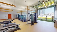 Located at 2 Harbor Point Road South in Stamford, CT, this state-of-the-art fitness center offers a comprehensive and well-appointed workout environment across a single floor. The facility is designed with an open, airy layout highlighted by soaring ceilings, exposed wooden beam accents, and abundant natural light streaming through floor-to-ceiling windows that frame sweeping views of the surrounding cityscape.

The main workout area is generously equipped with a full row of Matrix treadmills and elliptical machines, a dedicated free weights and strength training section featuring a power rack and dumbbell station, and a variety of selectorized cable and resistance machines. Bold orange accent walls and large wall-to-wall mirrors amplify the energy of the space while enhancing depth and visibility throughout.

A standout feature is the indoor-to-outdoor turf zone, seamlessly connected to the main floor via a retractable glass garage door. This astroturf section accommodates stationary bikes and functional training equipment, all bathed in natural sunlight with open city views.

A separate studio area with hardwood flooring, a large mounted display screen, and Matrix Pilates-style equipment provides a dedicated space for group classes or personal training. Additionally, a serene meditation room with floor-to-ceiling windows, sheer linen drapes, and a calming garden outlook offers a tranquil retreat for mindfulness and recovery.