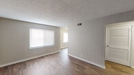 Located at 3715 Third Ave E in Tuscaloosa, Alabama, this single-story unit offers a clean, functional layout with a neutral color palette throughout. The living area is a notable feature of the space, showcasing wood-look vinyl plank flooring in a warm medium-brown tone and a distinctive vertical shiplap accent wall finished in a soft gray-white. A large window with horizontal blinds allows ample natural light to fill the room, while a textured popcorn ceiling adds a classic residential character. The open sightline connects the living area to adjacent spaces, enhancing the sense of flow throughout the floor plan.

The bedrooms are finished with wall-to-wall carpet in a neutral beige tone, providing a comfortable and quiet feel. Each bedroom includes a window with blinds for natural light and privacy, along with standard textured ceilings. One bedroom features two doors, likely providing access to a closet and a hallway or secondary entry point.

The bathroom is straightforward and functional, equipped with a tub-shower combination, a wall-mounted vanity with a white sink surface, and a mirrored medicine cabinet above. Tile flooring and neutral wall finishes keep the space clean and practical.

Throughout the unit, consistent white trim, neutral wall tones, and vinyl plank flooring in the main living areas create a cohesive, move-in-ready aesthetic.