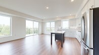 This thoughtfully designed two-bedroom, one-bathroom residence offers a bright and contemporary living experience across a single floor. The open-concept kitchen and living area serves as the heart of the home, featuring warm hardwood-style flooring, recessed lighting, and large windows that flood the space with natural light. Sliding glass doors lead to a private balcony, offering pleasant outdoor views of surrounding greenery.

The kitchen is well-appointed with crisp white shaker-style cabinetry, light quartz countertops, a gray subway tile backsplash, a deep stainless steel undermount sink, and a full suite of stainless steel appliances including a gas cooktop, double wall oven, refrigerator, and dishwasher. A central island with a contrasting dark base provides additional workspace and seating. The living room is anchored by a sleek fireplace with a wood-toned mantel and built-in shelving.

Both bedrooms are carpeted and finished in soft neutral tones. The spacious primary bedroom includes a walk-in closet with built-in shelving. A second bedroom features a tall vertical window with treetop views and additional built-in shelving. The full bathroom offers a tub-shower combination with white subway tile surround. A dedicated laundry room includes a full-size front-loading washer and dryer.