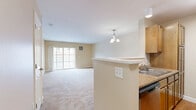 Located at 6 Timberwood Dr, Unit 303 in Lebanon, New Hampshire, this one-bedroom, one-bathroom residence offers a well-organized single-level layout with a warm, neutral color palette throughout. The open-concept living and dining area is finished with plush wall-to-wall carpeting and features a elegant chandelier that anchors the dining space. Large sliding glass doors flood the living room with natural light and provide access to an outdoor balcony with greenery views, enhancing the sense of openness. The galley-style kitchen is thoughtfully designed with warm wood cabinetry, granite-style countertops, hardwood-style flooring, and stainless steel appliances including a range, microwave, refrigerator, and dishwasher — all accessible via a convenient pass-through counter that connects to the living area. The bedroom is a comfortable retreat featuring soft carpeting, a generous window with outdoor views, and direct access to a dedicated closet. The full bathroom includes a clean, bright tub and shower combination with tile flooring. White panel doors, crisp baseboards, and consistent warm beige walls throughout lend the space a cohesive and move-in-ready appeal.