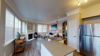 This single-floor residence offers a thoughtfully designed layout with a cohesive blend of wood-look flooring, neutral tones, and classic architectural details throughout. A central hallway with flush ceiling lighting connects the main living areas, with decorative wall art adding character to the passage.

The living room is a standout space, anchored by a white-framed fireplace and flanked by built-in shelving accessible through an arched entryway. Large windows flood the room with natural light, while crown molding adds a refined touch. Adjacent to the living area, a bay window dining nook provides an intimate setting with abundant natural light on multiple sides.

The kitchen features white shaker cabinetry, dark countertops, stainless steel appliances including a refrigerator, dishwasher, and microwave, and a peninsula that opens toward the main living space. A dedicated laundry area houses a full-size washer and dryer with overhead wire shelving for storage.

The primary bedroom includes plush carpeting and a bold patterned accent wall, creating a distinctive focal point. A second bedroom offers carpeted flooring and a ceiling fan. The full bathroom is finished with white cabinetry, a dark countertop, and a tub-shower combination.