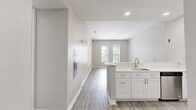 This 770-square-foot, single-floor apartment at Bradlee Danvers in Danvers, MA features 2 bedrooms, 1 bathroom, a combined kitchen and living room, and a hallway. The unit is finished with light wood-style luxury vinyl plank flooring and neutral gray walls throughout, creating a clean, contemporary aesthetic. The open-concept kitchen flows into the living area and is outfitted with white shaker cabinetry, quartz countertops, a peninsula with bar seating, stainless steel appliances including a gas range, microwave, dishwasher, and refrigerator, plus recessed lighting. The primary bedroom measures 140 square feet and features two windows with blinds that allow ample natural light. The second bedroom also includes dual windows, offering outdoor views and bright, airy feel. Closet storage features wire shelving systems for organized storage. The bathroom is appointed with a white shaker vanity, quartz countertop, framed mirror, wall-mounted medicine cabinet, and wood-style flooring consistent with the rest of the unit. A hallway connects the living areas to the bedrooms and bathroom, providing a functional and well-organized floor plan suited for comfortable everyday living.