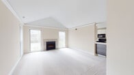 This single-floor residence is defined by its vaulted ceilings and neutral palette, creating a bright and open atmosphere throughout. The main living area is generously proportioned, featuring plush wall-to-wall carpeting, crisp white crown molding, and a tile-surround fireplace that serves as a focal point. Large sliding glass doors and vertical-blind windows allow abundant natural light to fill the space while providing outdoor views.

The kitchen is designed for functionality, offering a galley-style layout with high-gloss white upper cabinetry, dark lower cabinets, and stainless steel appliances including a refrigerator, range, and built-in microwave. White tile flooring and a sliding glass door at the end of the kitchen add brightness. A pass-through counter connects the kitchen to the living area, enhancing the open-concept flow.

Bedroom areas feature soft carpeting and well-proportioned closets with bifold doors providing ample storage. Two bathrooms serve the unit: one features a modern floating white vanity, a wide mirror cabinet with integrated shelving, and clean lines; the other offers a full soaking tub with white tile surround and shower curtain. Both bathrooms maintain a consistently clean, minimal aesthetic with light-toned finishes throughout.