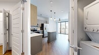 Located at 1001 16th Ave S in Nashville, TN, this two-bedroom, one-bathroom unit offers a well-designed layout across a single floor. The open-concept kitchen serves as a centerpiece, featuring two-tone cabinetry with light wood uppers and slate-blue lower cabinets, quartz countertops, a herringbone-patterned tile backsplash, and a full suite of stainless steel appliances including a French door refrigerator, electric range, built-in microwave, and dishwasher. A central kitchen island provides additional prep and seating space. Wood-look flooring runs throughout the unit, contributing to a cohesive, contemporary aesthetic. The living area extends toward a floor-to-ceiling glass sliding door that opens to a private balcony, allowing abundant natural light. The primary bedroom offers a comfortable footprint with a ceiling fan and dedicated closet space, while a second bedroom provides flexible use. Two closets, including a walk-in with wire shelving, add practical storage. The bathroom includes a soaking tub with marble-style tile surround, a quartz vanity with gray cabinetry, and wood-look flooring, maintaining the modern finishes found throughout the unit.