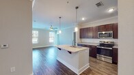 Located at 9110 Crowne Springs View in Colorado Springs, Colorado, this well-appointed single-floor residence offers a thoughtfully designed open-concept layout with modern finishes throughout. The kitchen serves as a central focal point, showcasing rich dark-wood cabinetry, granite countertops, a subway tile backsplash, and a full suite of stainless steel appliances including a range, microwave, and refrigerator. A kitchen island with a built-in sink, pendant lighting, and bar seating provides both functionality and style, flowing seamlessly into the living area, which features crown molding, a ceiling fan, and access to a private balcony through a glass door. Durable wood-style flooring runs throughout the main living spaces, while plush carpet adds warmth to the bedrooms. Each bedroom is generously proportioned, fitted with ceiling fans and natural light from large windows. The primary bathroom includes a granite-topped vanity with dark cabinetry, wood-style flooring, and a walk-in closet with built-in shelving. A secondary bathroom offers a tub-shower combination and coordinating finishes. The neutral color palette and crown molding details give the entire residence a clean, cohesive aesthetic.
